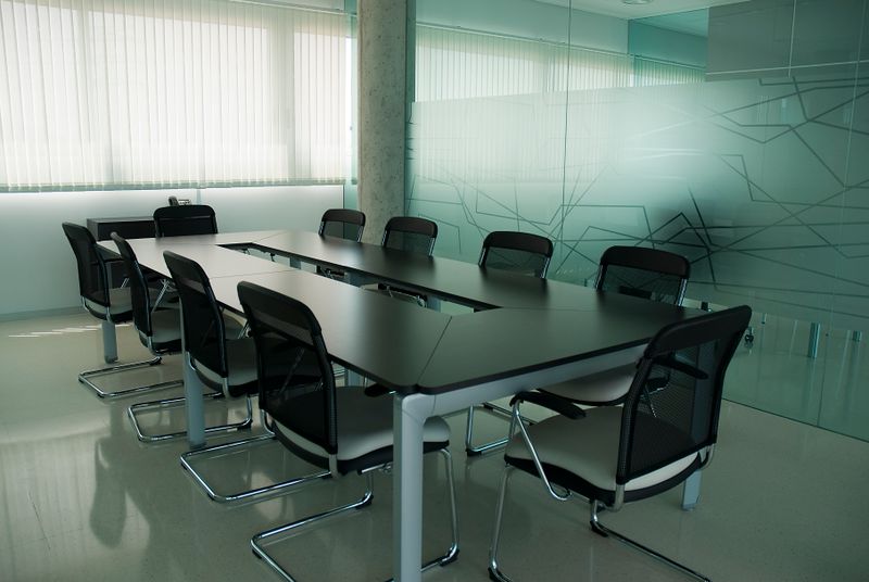Salle de réunion executive, table longue sobre, chaises cuir, lumière tamisée