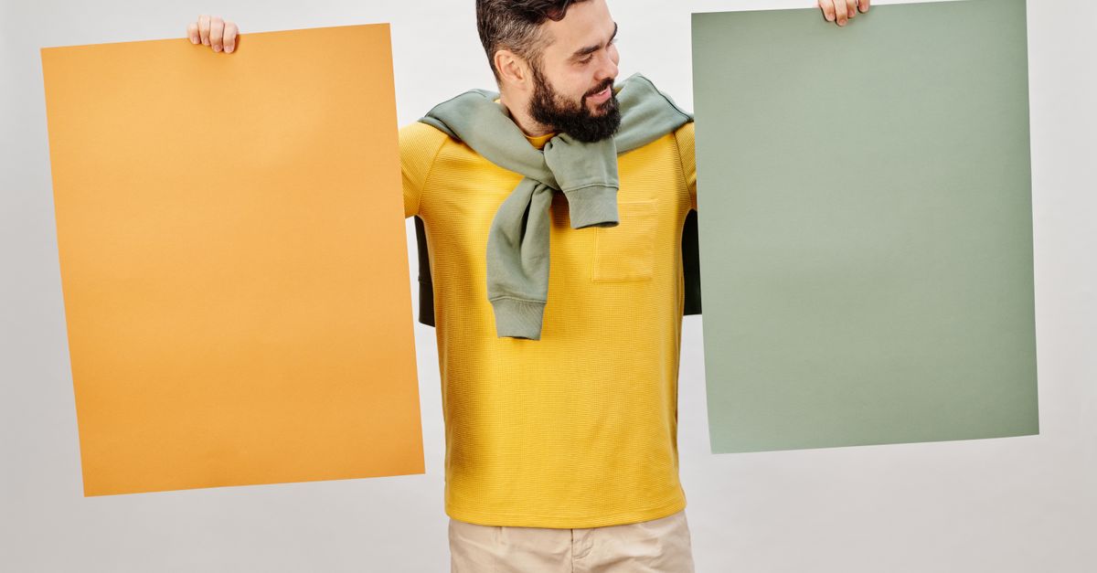 Bearded man in yellow shirt holding blank orange and green posters with copyspace.