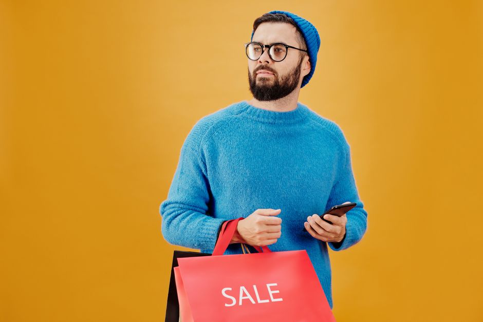 Stylish man in blue holding sale bags and smartphone, looking away. Stylish man in blue holding sale bags and smartphone, looking away.