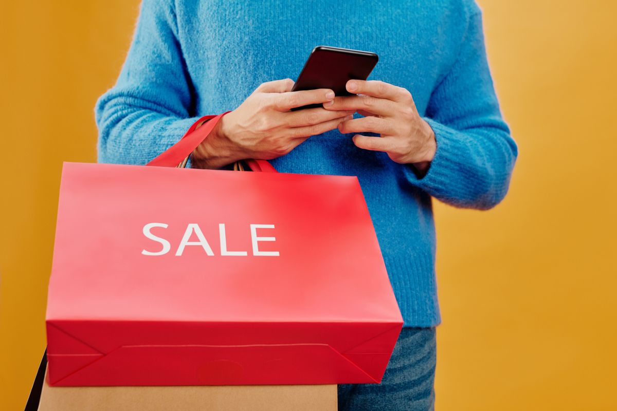 Shopper holding a red sale bag while checking a smartphone