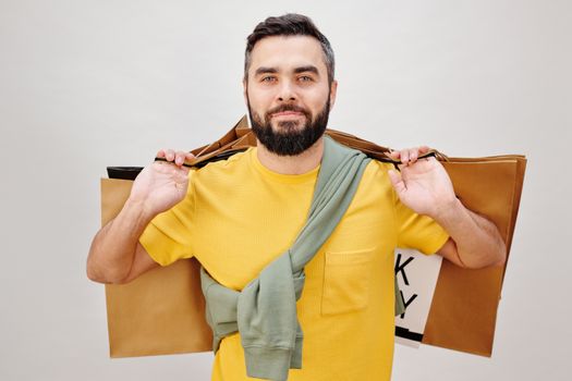 一位留着胡须、身穿黄色衬衫的男子拿着购物袋，背景中立