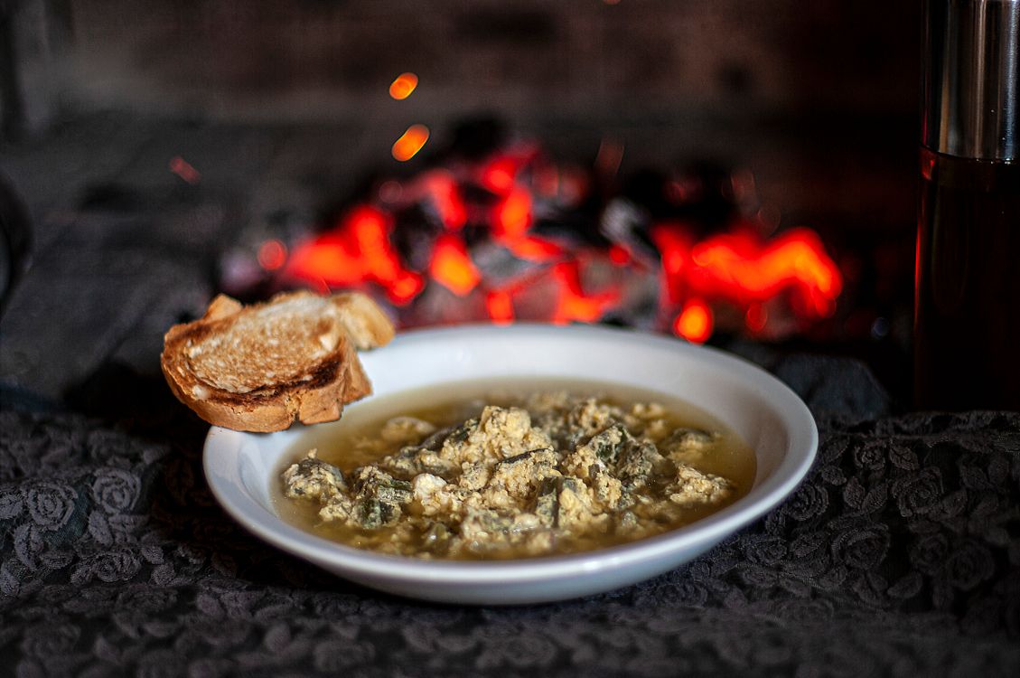 Best soups for winter: a warm bowl of soup with toast served by a cozy fire