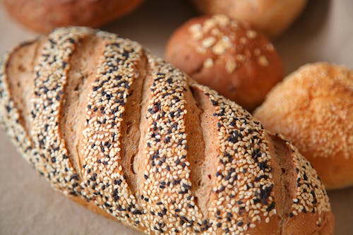 High angle of fresh baked bread with soft buns with sesame seeds served on surface in light place