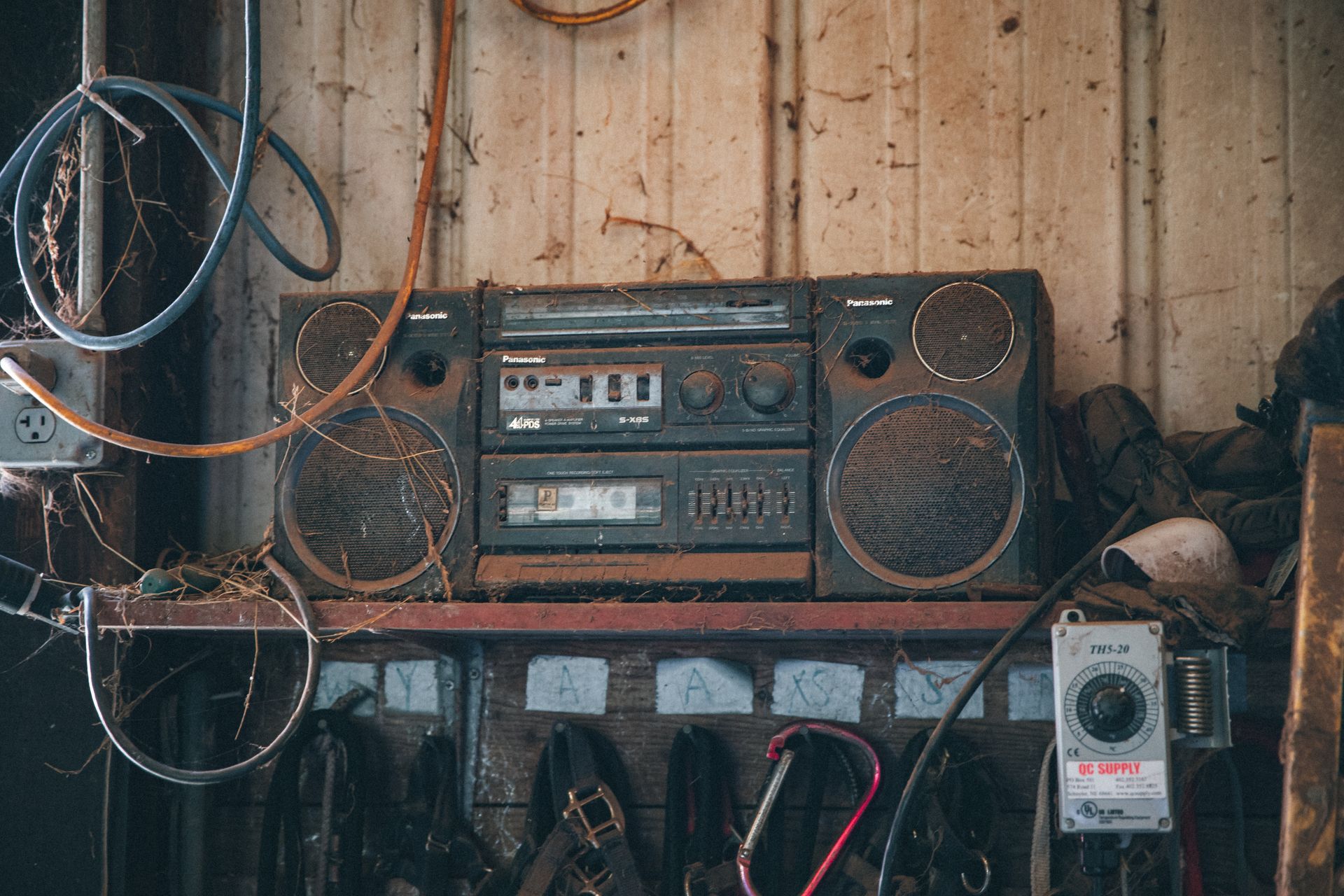 Old fashioned obsolete compact stereo system covered with dust placed on shelf near wooden wall in workshop with tools and wires
