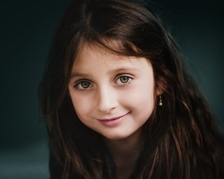 Positive girl with gentle smile and long dark hair wearing earrings and looking at camera
