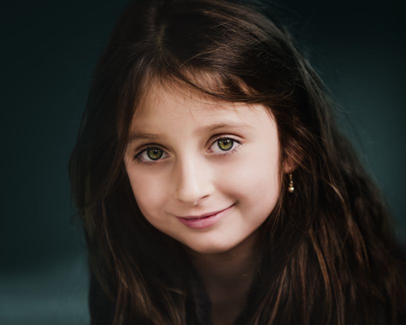 Positive girl with gentle smile and long dark hair wearing earrings and looking at camera
