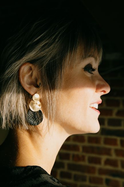 Side view of young cheerful female with makeup in contemporary earring looking forward in sunlight