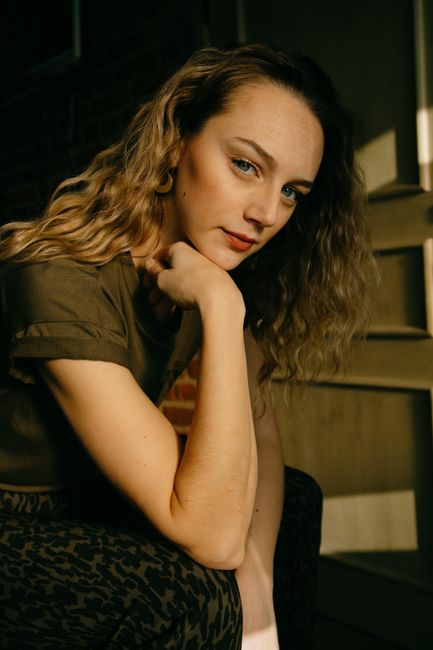 Portrait of a reflective woman resting her chin on her hand in gentle light.