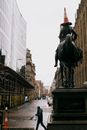 Old stone sculpture on pedestal near road with unrecognizable man and multistage house facades in Glasgow