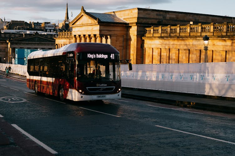 Contemporary Bus Driving On City Road Near Old Buildings