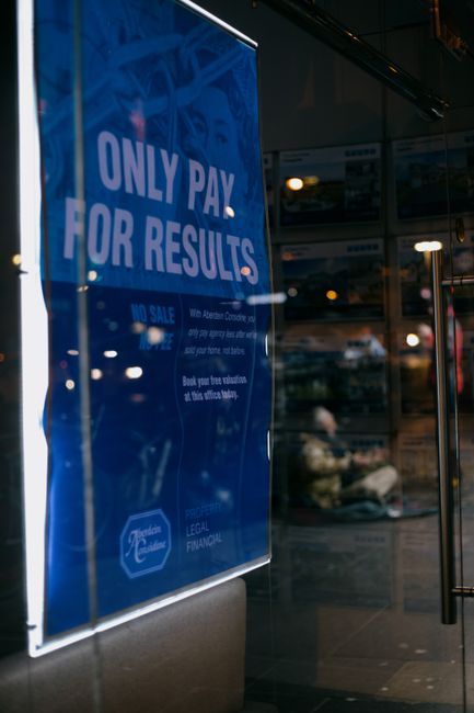 Street placard with information near glass door reflecting town illuminated by shiny lights in evening