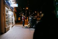 Anonymous man giving money to poor beggar on tiled sidewalk near shop showcases in town at dusk