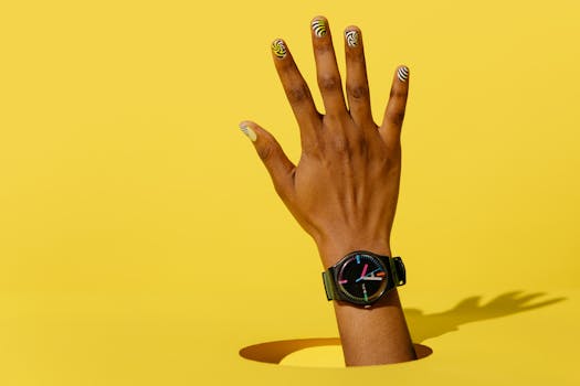 A hand adorned with a smartwatch and vibrant nail art emerges from a hole in a minimalist yellow backdrop.