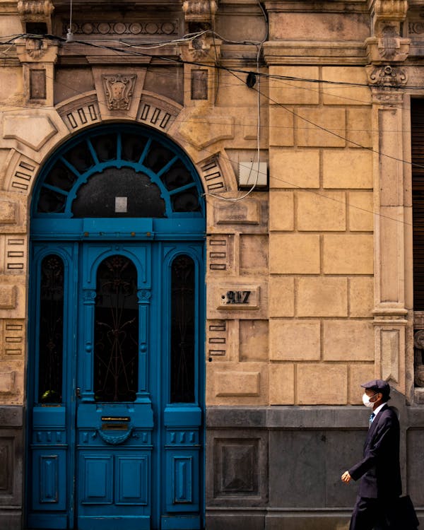Man in Black Suit Walking in Front of Blue Wooden Door
