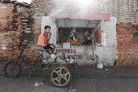 Ethnic boy sitting on aged tricycle near poor street stall