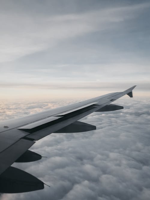 Wing of airplane flying over clouds at sundown