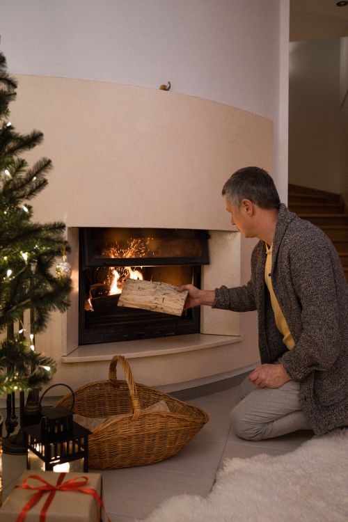 Free A man adds firewood to a fireplace, creating a warm, cozy indoor scene during winter. Stock Photo