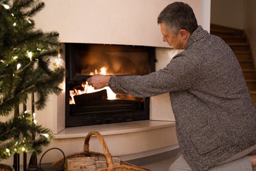 Man in Gray Sweater Standing in Front of the Fireplace