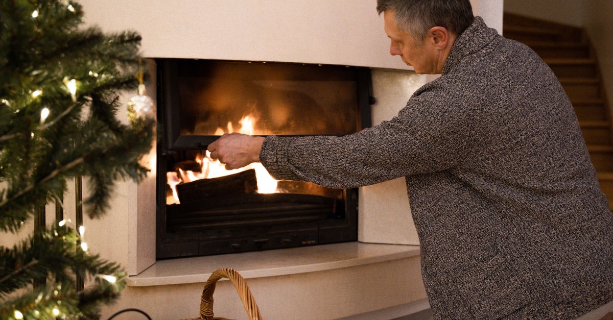 Man tending to a warm fireplace in a cozy home setting during winter.