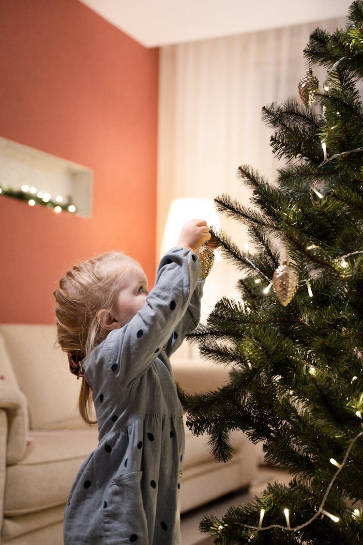 Cute Kid Hanging Christmas Decorations On A Christmas Tree