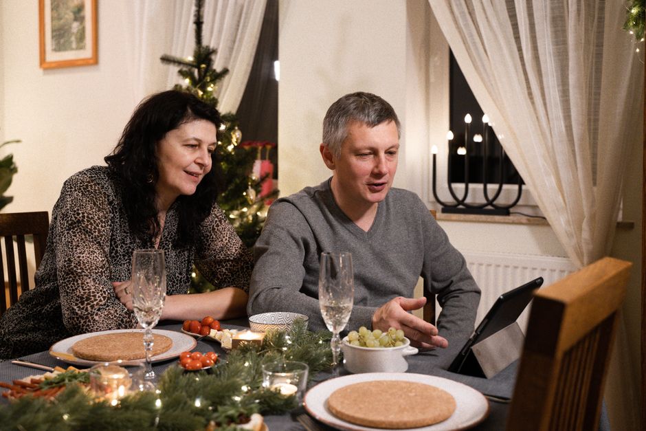A couple enjoys a video call during a holiday dinner at home, surrounded by festive decor.