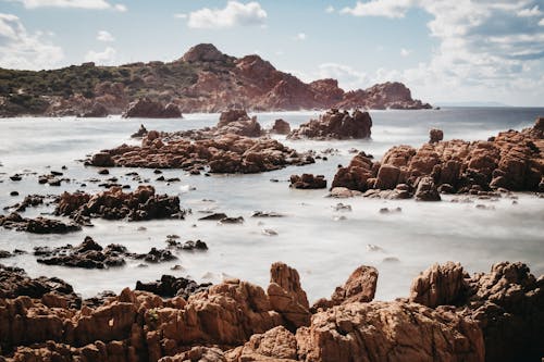 Picturesque landscape of rough rocky formations and cliffs in wavy ocean against cloudy blue sky