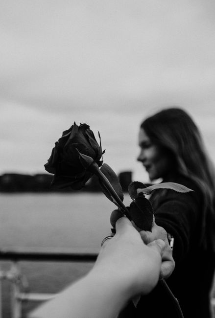 Crop anonymous man giving elegant rose to young happy girlfriend relaxing on embankment near lake during romantic date