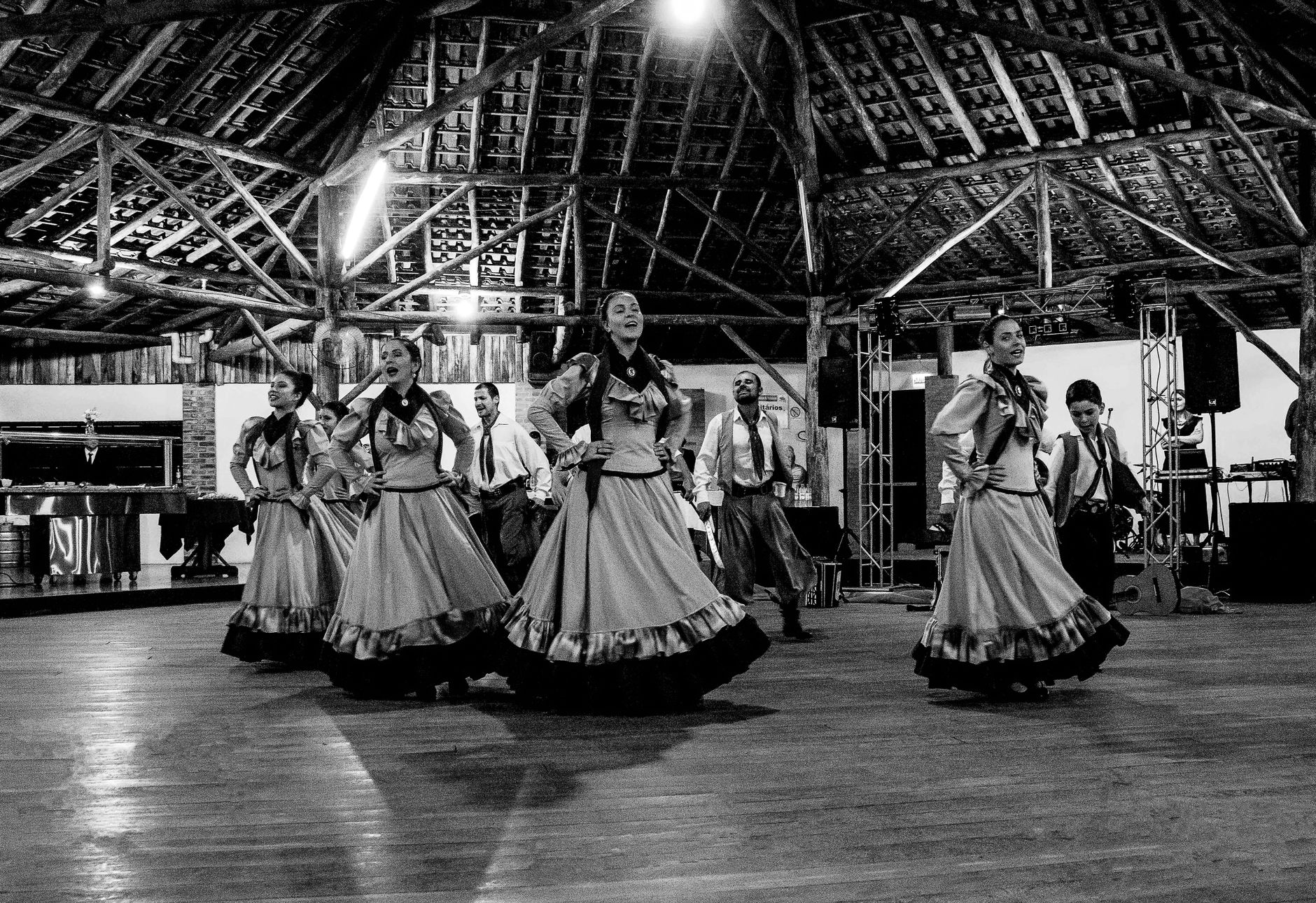 Black and white image of a cultural dance performance in a rustic indoor setting.
