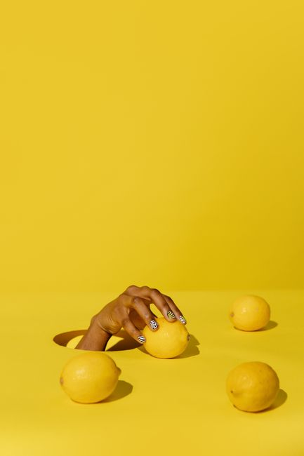 A hand emerges through yellow background with lemons, offering vibrant creativity and citrus freshness.