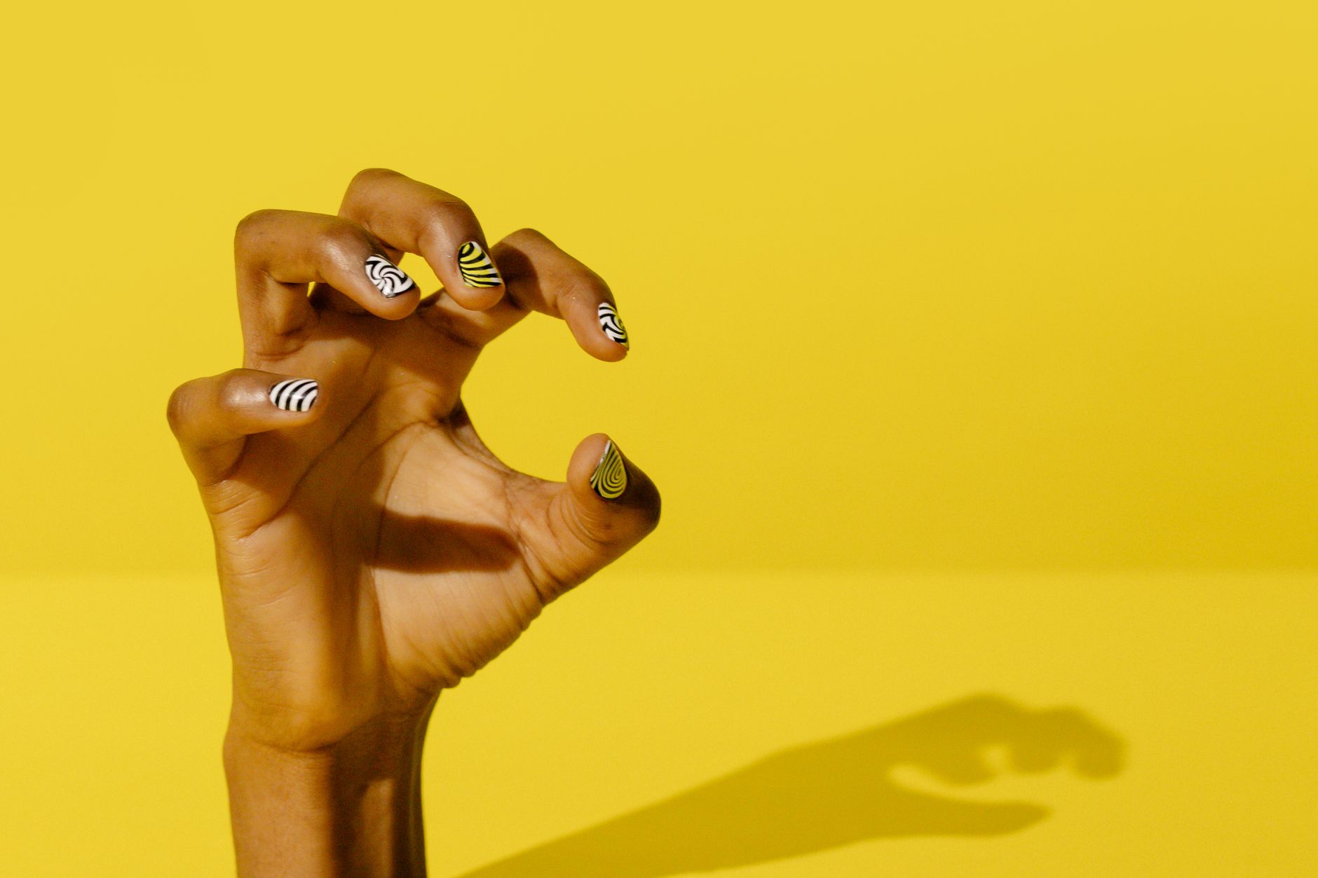 Close-up of a hand with artistic nail polish against a yellow background.