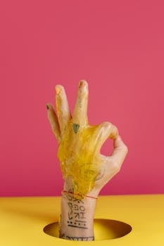 Close-up of a tattooed hand doing OK sign covered in goo with a vibrant background.