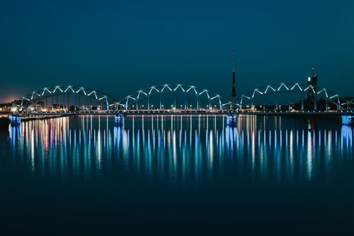 Free Illuminated historic arched iron Railway Bridge reflecting in river water against cloudless night sky in Riga Stock Photo