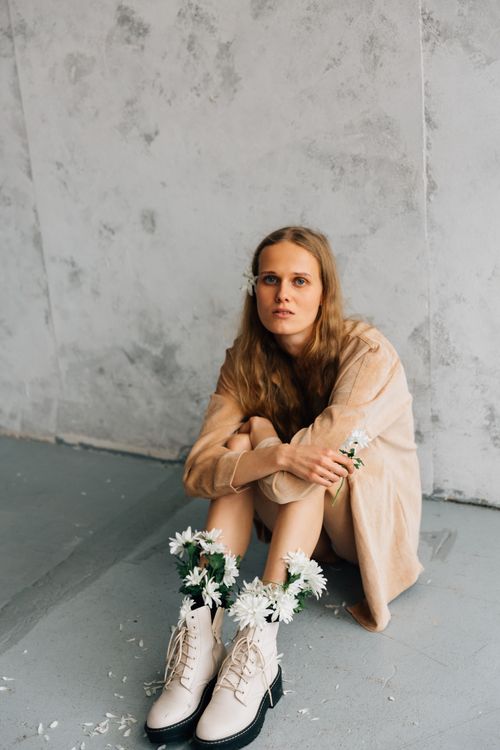 Free Fashionable woman in beige coat sitting indoors with floral embellished boots. Stock Photo