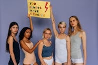 Women in Tank Tops Standing Near the Purple Wall while Holding a Banner