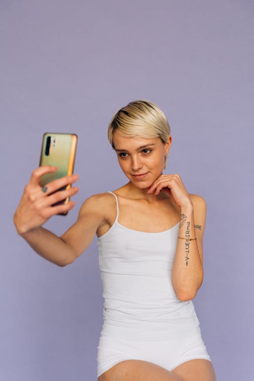 無料 ゴールドのi Phone6を保持している白いタンクトップの女性 写真素材