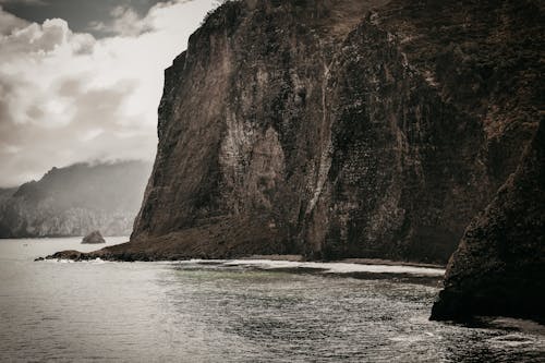 Amazing landscape of huge rocky cliff in rippling sea with foamy waves against overcast sky