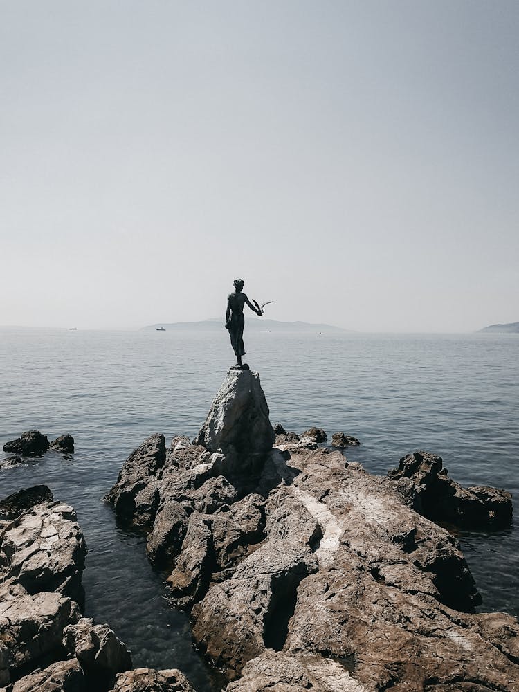 Woman Statue On Rocky Cliff In Sea