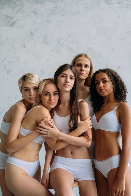 Five diverse women embracing in a powerful display of unity and strength against a neutral background.