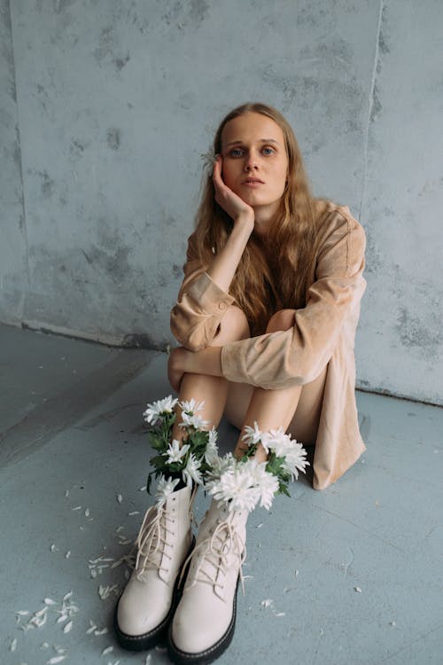 A Woman in Brown Long Sleeves Wearing Boots with White Flowers while Sitting on the Floor