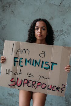Young woman confidently holding a feminist empowerment sign against textured wall.