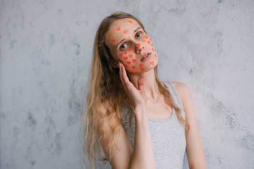 Artistic portrait of a woman with heart stickers on her face against a textured wall.