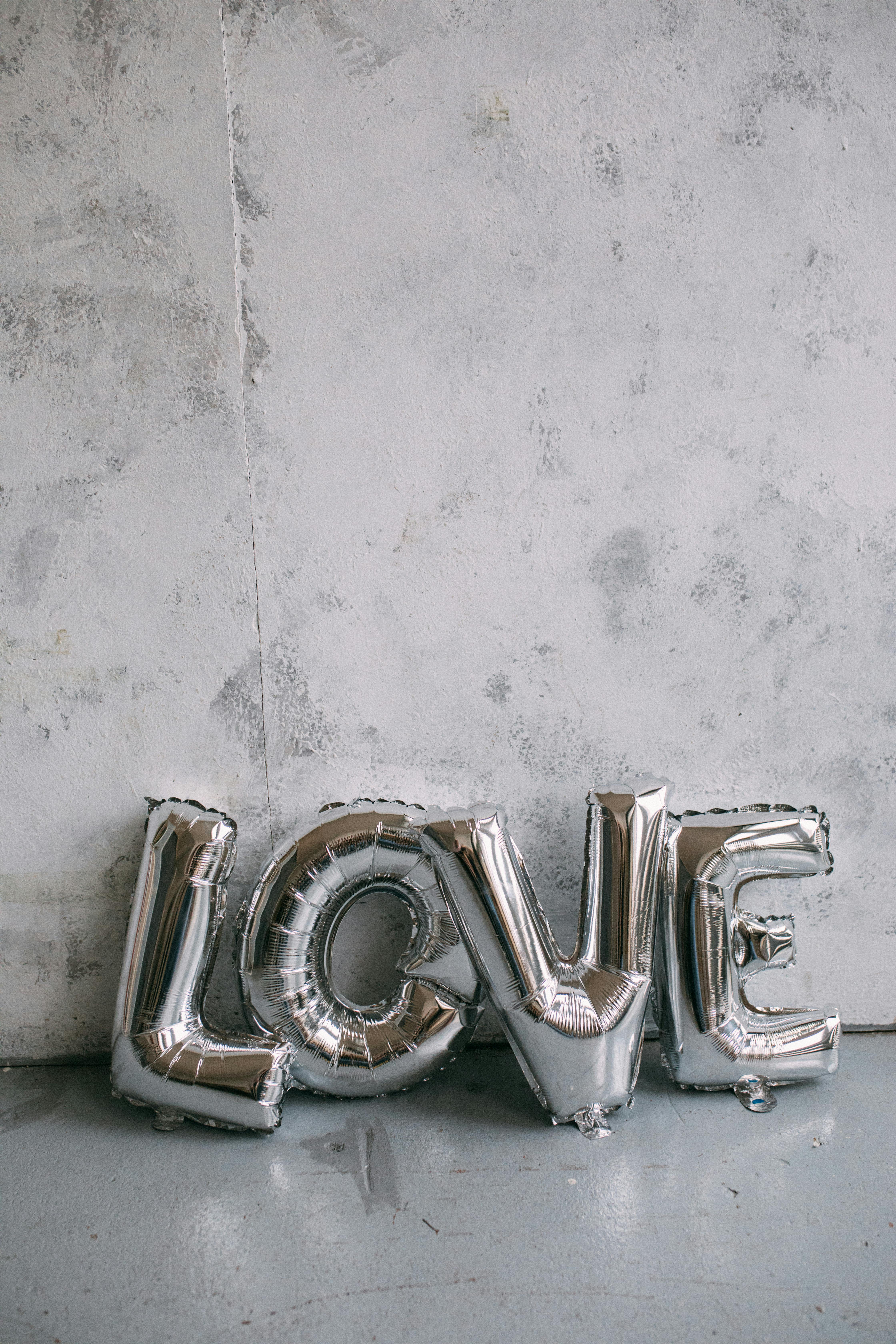 Silver metallic letter balloons spelling 'LOVE' against a textured wall, perfect for events and decorations.