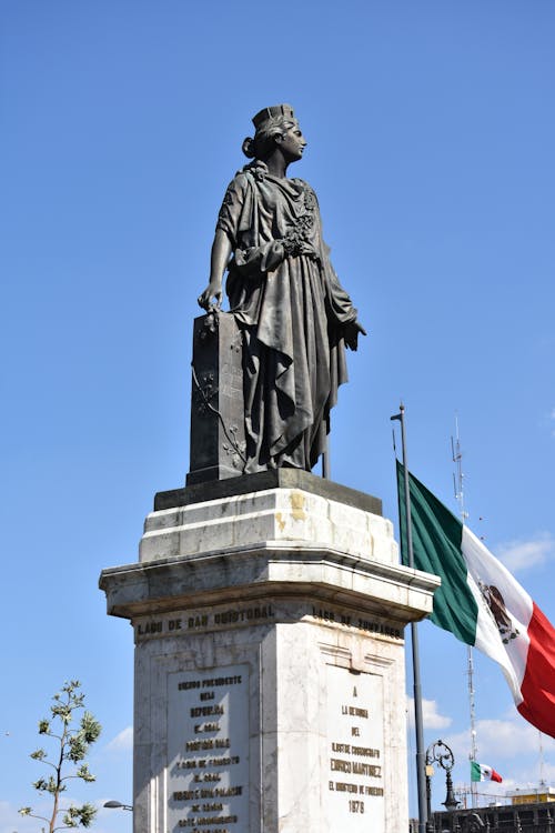 Free Statue of a Woman on a Pedestal Near Mexican Flag Stock Photo