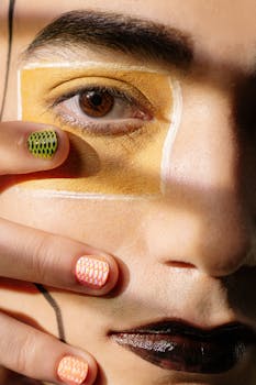 Close-up portrait highlighting creative eye makeup and colorful nail art, showcasing artistic expression.