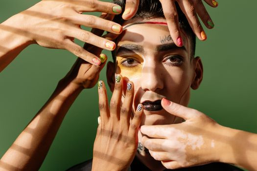 Artistic portrait showcasing bold makeup, colorful nails, and diverse hands on a green background.