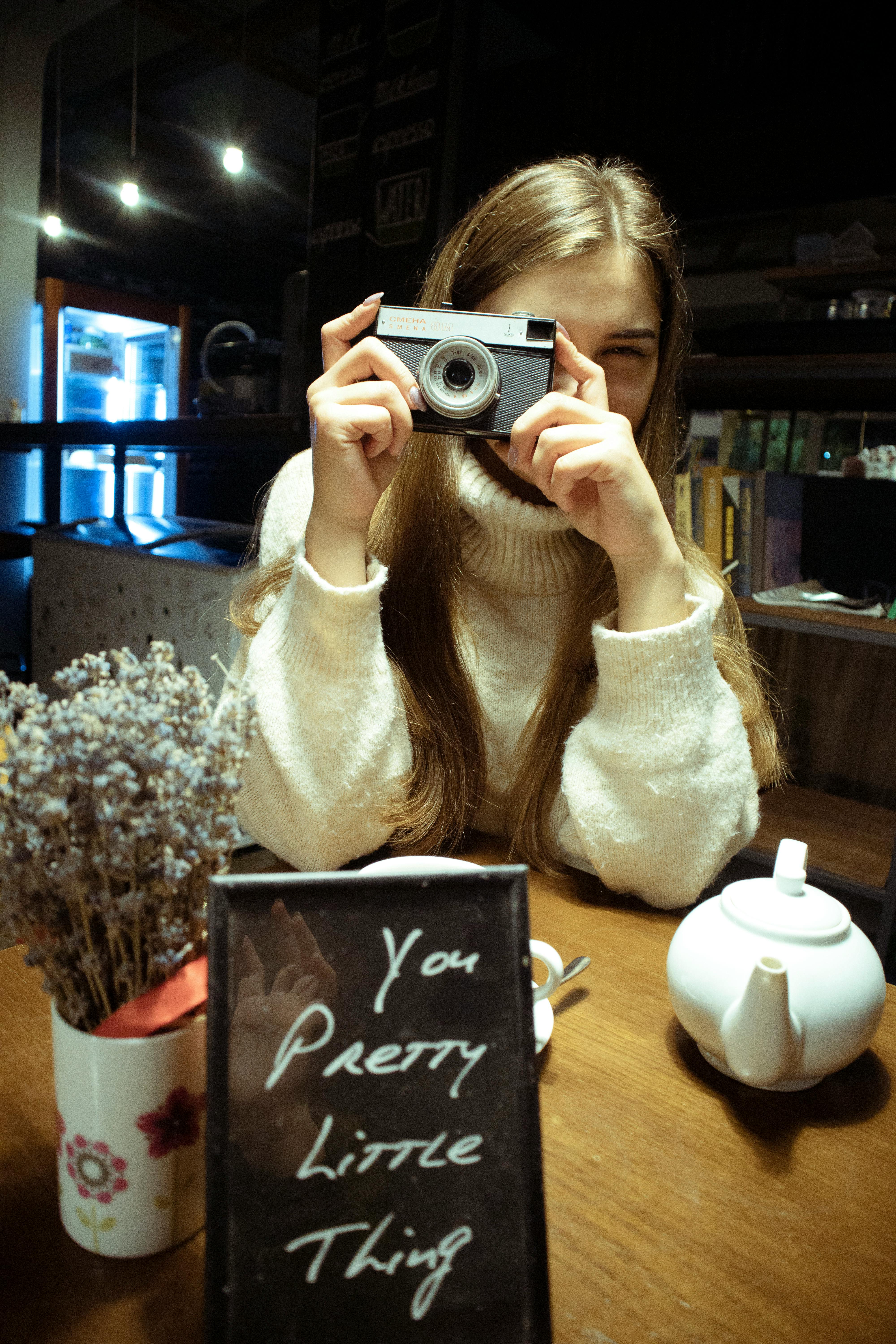 Woman in a sweater taking a photo in a cozy cafe with a vintage camera.