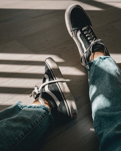 Free From above of crop anonymous person in trendy sneakers and jeans resting on parquet floor in sunlight Stock Photo