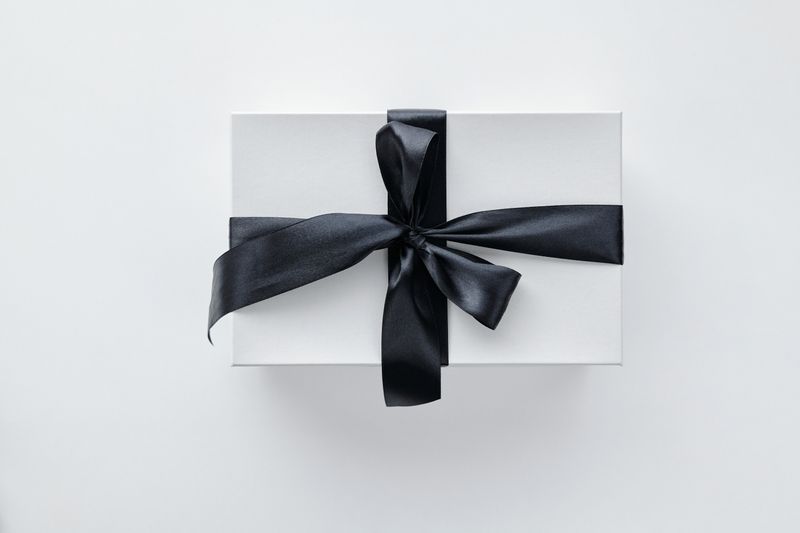 Top view of closed black gift box with gold ribbon accents on white surface