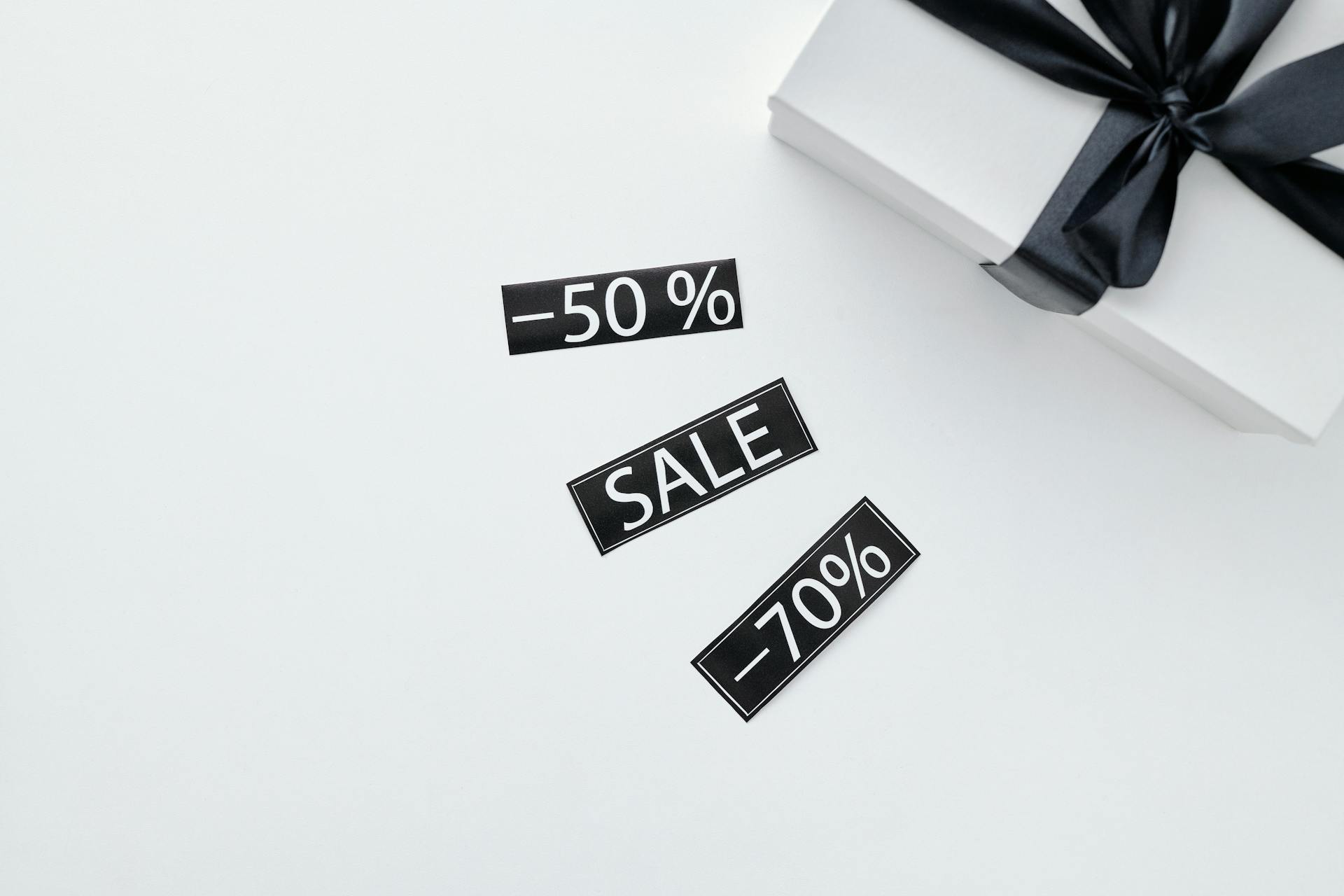 Elegant gift box with black ribbon on marble surface alongside sale discount stickers, perfect for promotional materials.