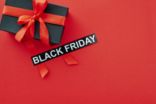 Free Black Friday sale concept with a gift box and red ribbon on vibrant red background, ideal for promotional use. Stock Photo